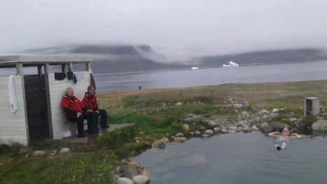 One pax enjoys a natural warm water spa at Uunartoq, south Greenland as 2 e