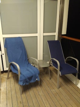 Balcony at night with outside light on showing 2 deck chairs with table.