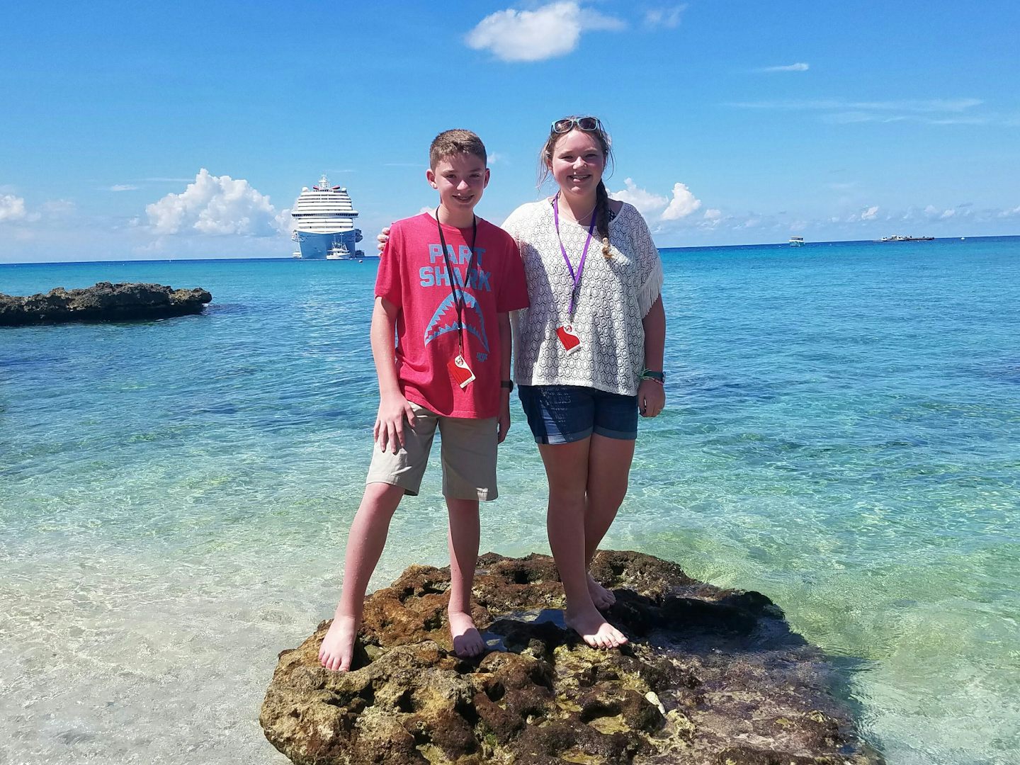 My kiddos standing on a rock formation in Grand Cayman with our ship,  The Carnival Breeze in the background.