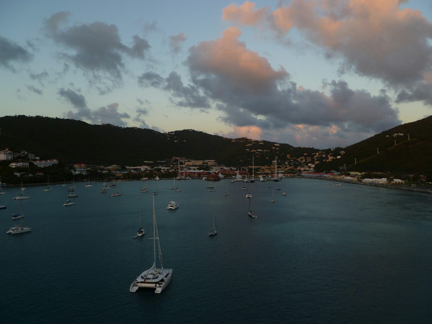 Boats anchored in port in St. Thomas, USVI while the ship sails away at sunset