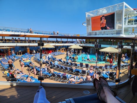 Relaxing on lounge chairs around the Lido deck pool with giant screen TV overhead.